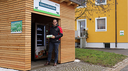 Ein Mann steht vor einem Häuschen, in dem ein Verkaufsautomat aufgebaut ist