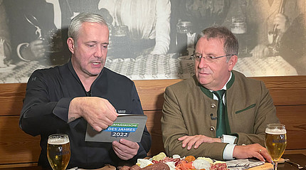 Zwei Männer sitzen an einem Tisch und öffnen einen Umschlag