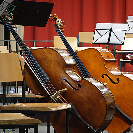 Zwei Cellos im Vordergrund, dahinter stehen leere Stühle und Notenständer.