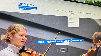 Auf einem Computerbildschirm ist eine Homepage zu sehen, darauf ein Bild von einer jungen Geigenspielerin. In der linken oberen Ecke steht der Schriftzug Haus Marteau