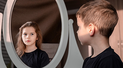 Ein Junge blickt in einen Spiegel und sieht darin ein Mädchen.