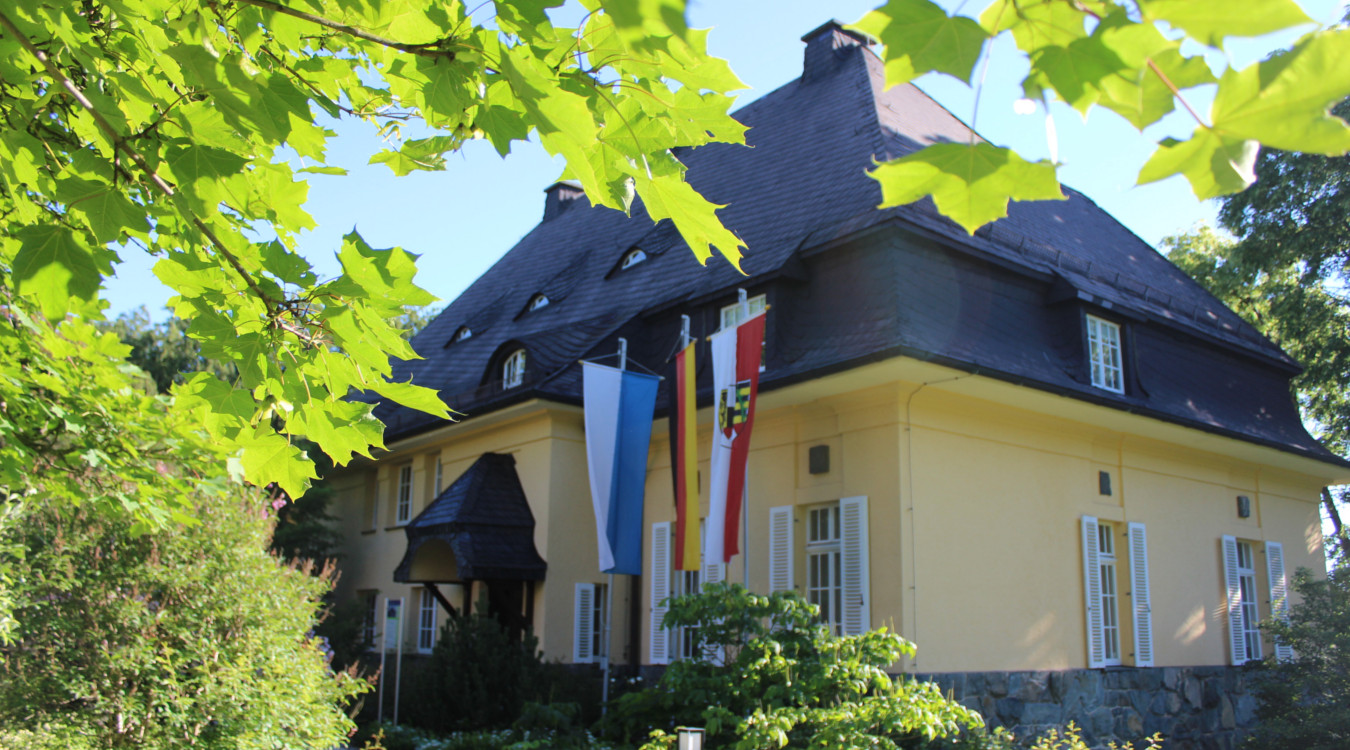 Idyllisch präsentiert sich die denkmalgeschützte Villa des ehemaligen Geigers, Henri Marteau, in Lichtenberg auf dem Bild. Vor der gelb gestrichene Villa aus dem Jahr 1913 mit weißen Fenstern und schwarzem Dach stehen drei Fahnenmasten mit der Fahne der B