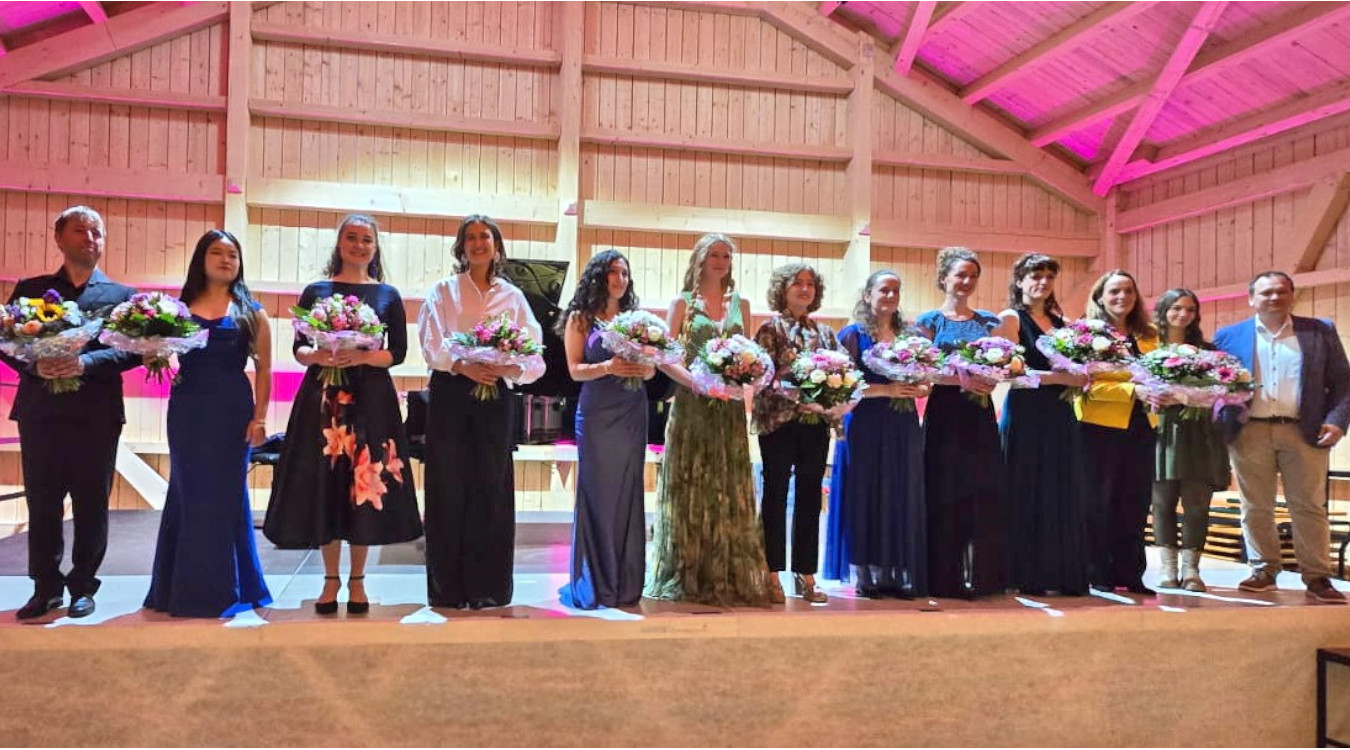 Elf Frauen mit Blumensträußen und zwei Männer stehen nebeneinander auf einer Bühne.