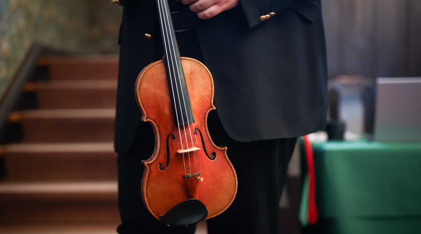 Violine Ausschnitt: Ein Mann im Anzug, der eine Geige hält.