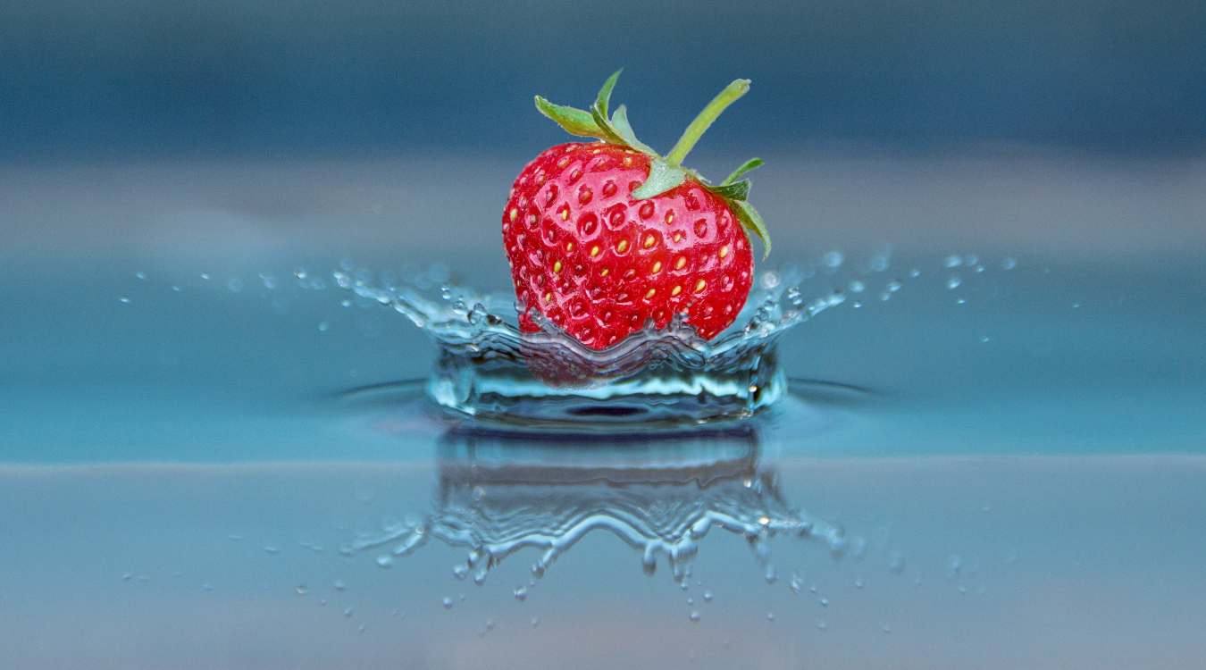 Man sieh eine Erdbeere, die zur Hälfte in Wasser "getaucht" wird. 