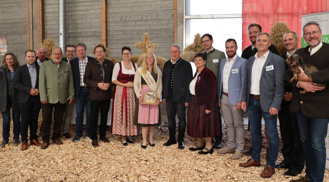 Eine Gruppe von etwa 20 Menschen steht nebeneinander. Sie tragen traditionelle Kleidung, zwei Frauen in der Mitte tragen Tracht. Eine junge Frau hat eine Krone auf dem Kopf.