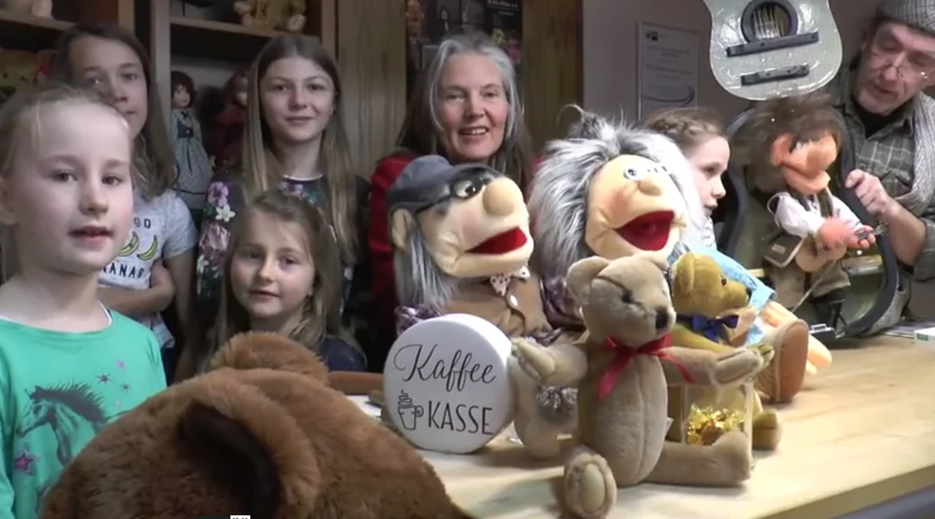Das Bild zeigt die Musikerin Kristina Jakobs im Spielzeugmuseum mit ihrem Kinderchor und Kuscheltieren. 