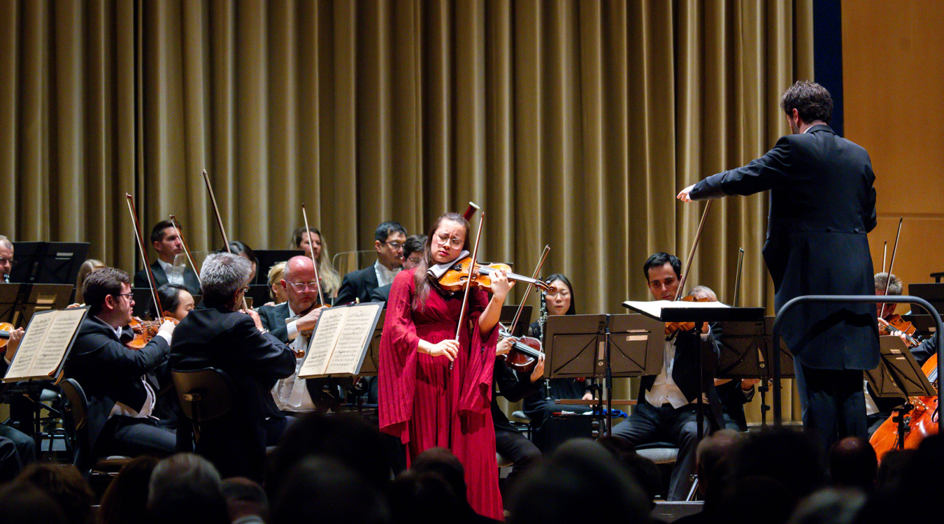 Maya Alexandra Kasprzak Eine Frau in einem roten Kleid, die Violine spielt.