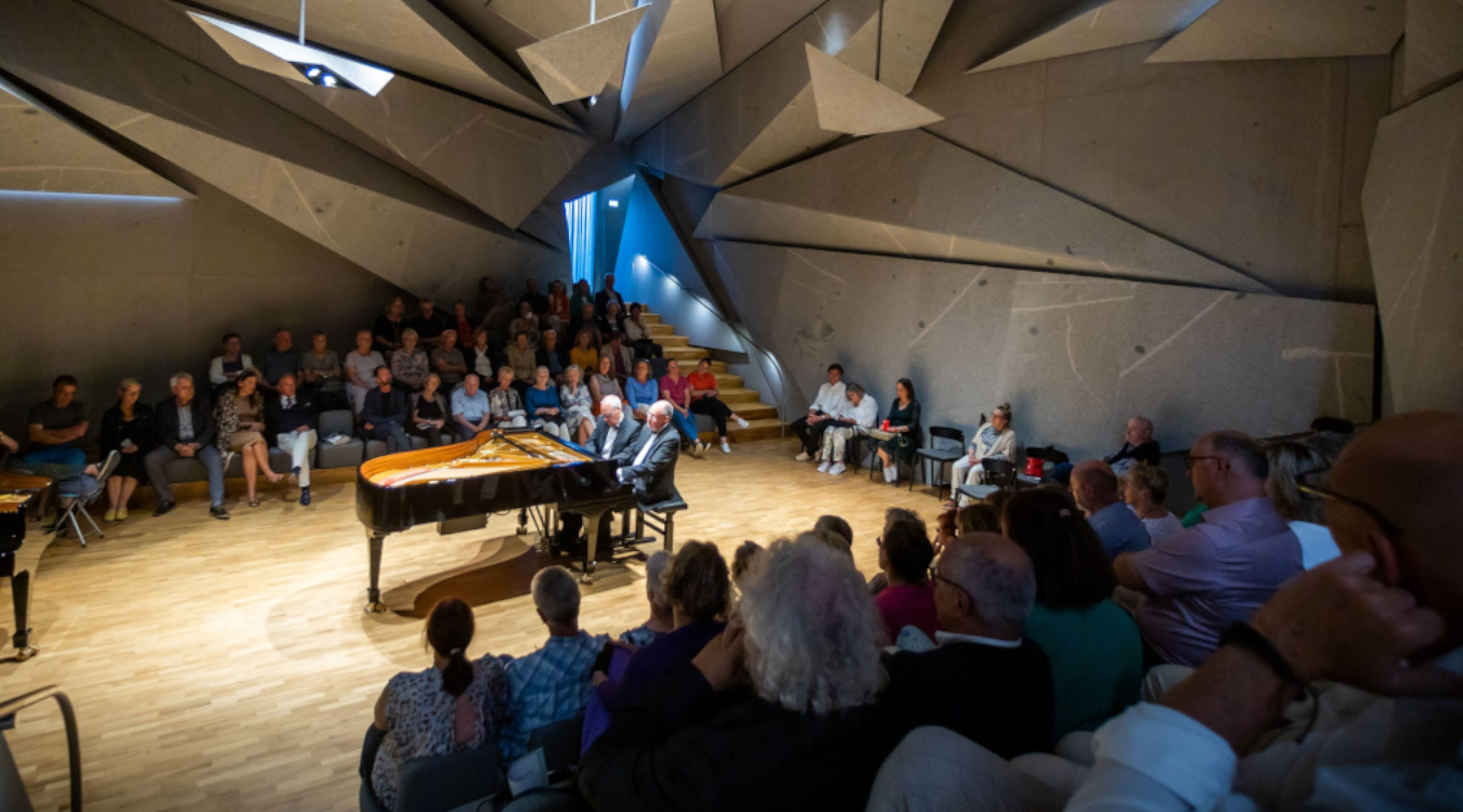 Meisterkonzert in Haus Marteau In der Mitte eines voll besetzten Konzertsaals sitzen zwei Männer an einem Flügel.