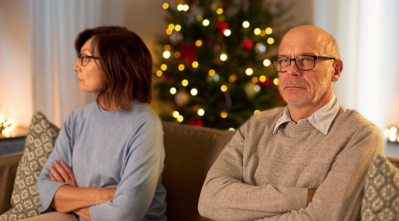 Eine Frau und ein Mann sitzen vor einem Weihnachtsbaum und sehen verärgert aus.