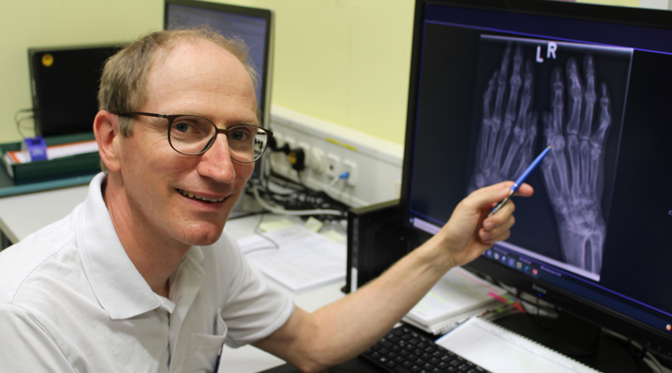 Rheumatologe Dr. Dirk Günthel Ein Mann mit Brille zeigt auf einen Arztbefund auf einem Bildschirm.
