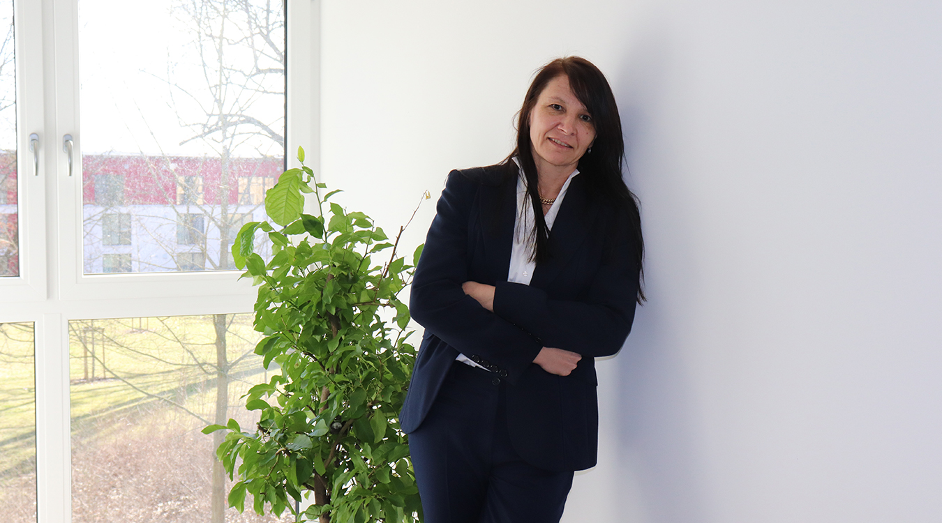 Marianne Witton Eine Frau, die einen Blazer trägt, steht vor einer Pflanze.