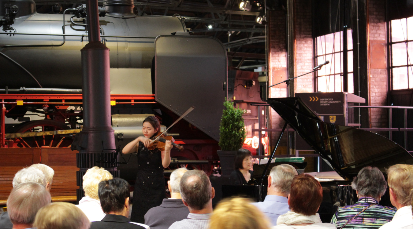 In einem alten  Industriebau spielt eine junge Violinistin vor Publikum Geige.