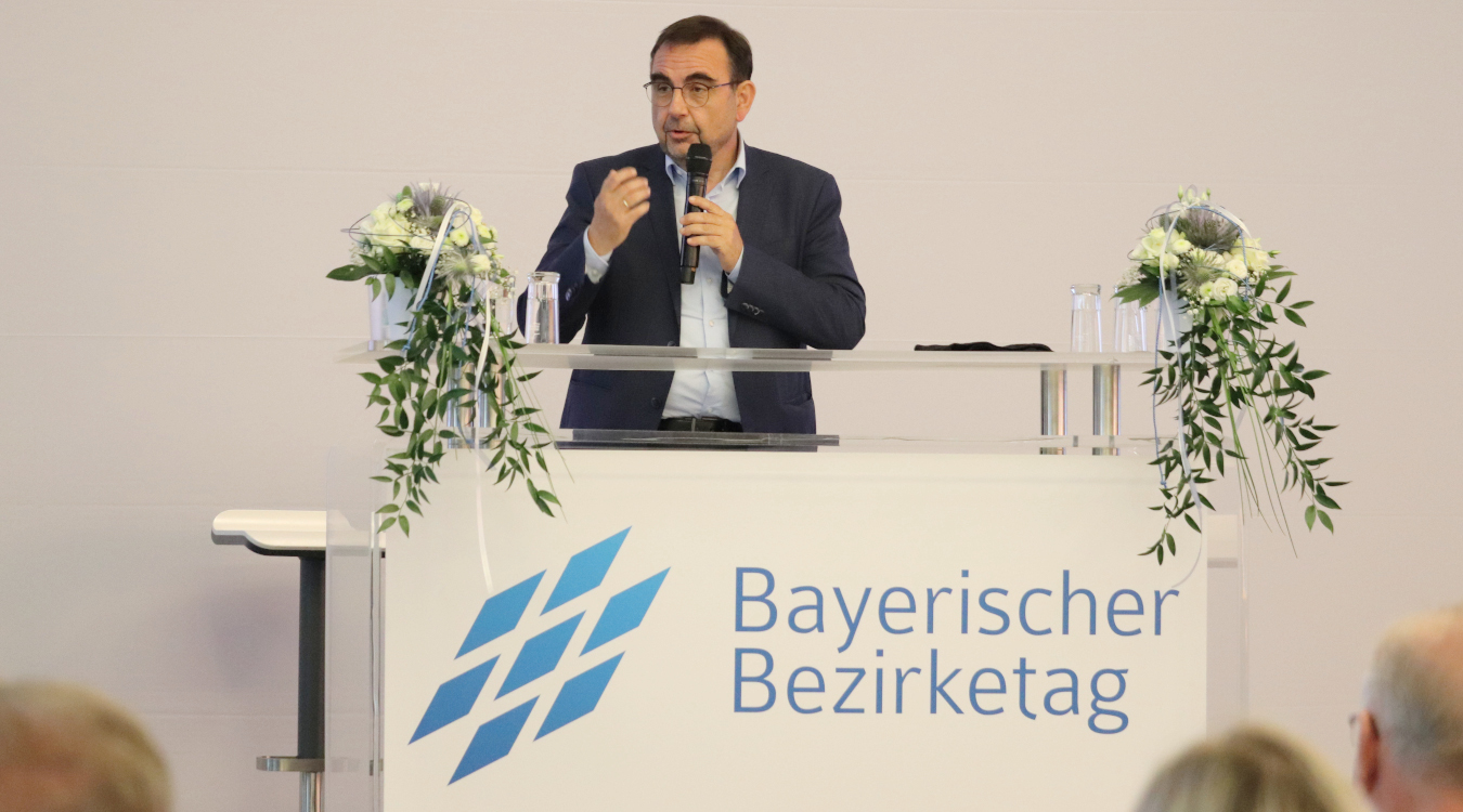 Ein Mann im Anzug steht an einem Rednerpult. Auf dem Pult steht die Aufschrift "Bayerischer Bazirketag"