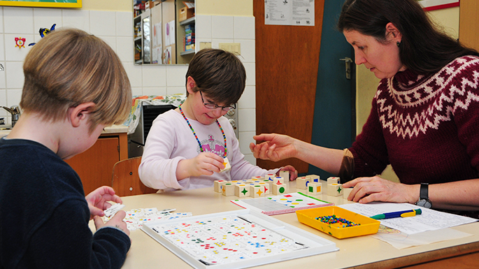 Eine pädagogische Fachkraft spielt mit zwei Kindern am Tisch ein Spiel.