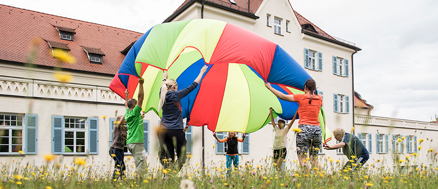 Eine Trainingsgruppe der Ergo- und Bewegungstherapie spielt auf einer Wiese des Bezirksklinikums Obermain in Kutzenberg mit einem großen bunten Tuch.