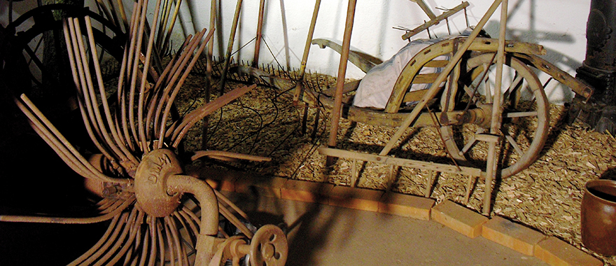 Alte Arbeitsgeräte aus der Landwirtschaft stehen in einer Scheune.