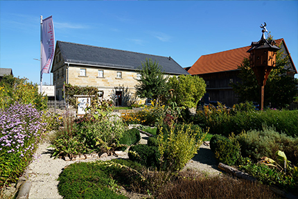 Das Bild zeigt den Kräutergarten der Hummelstube mit dem Museumsgebäute im Hintergrund 