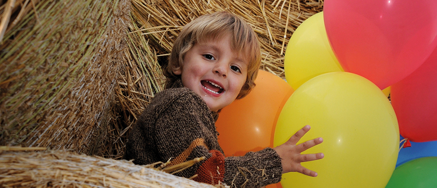 Ein Kind sitzt im Stroh und spielt mit bunten Luftballons