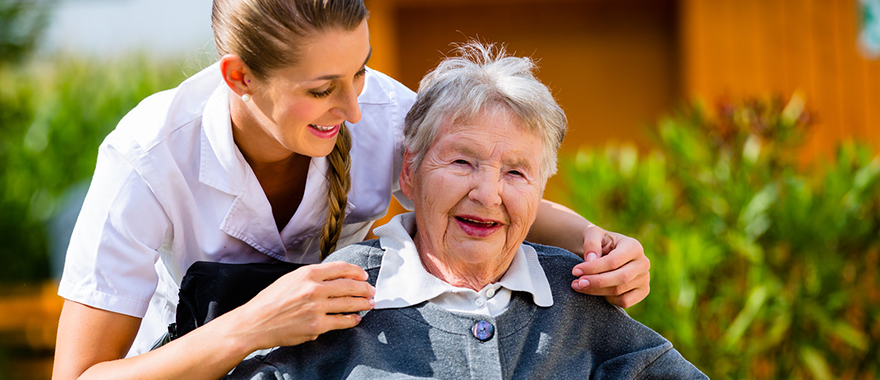 Eine Seniorin genießt gemeinsam mit ihrer Pflegerin den Sonnenschein im Garten eines Pflegeheims.