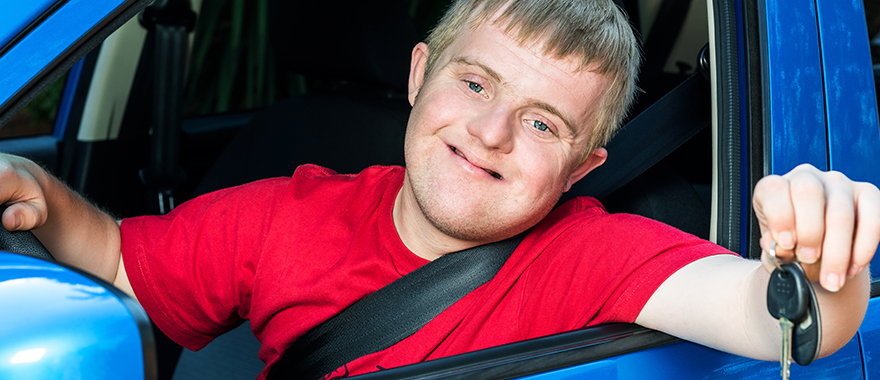 Ein junger Mann mit Down-Syndrom sitzt in einem Auto.